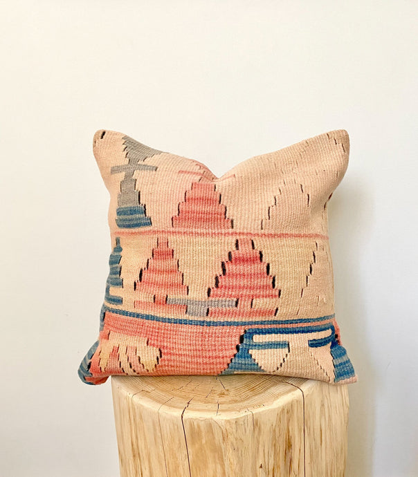 A square, kilim pillow cover with a geometric pattern in peaches and blues.