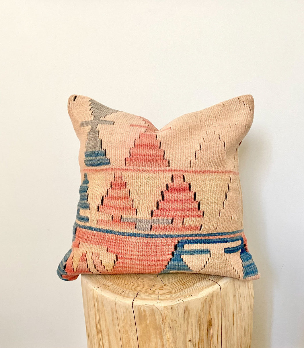 A square, kilim pillow cover with a geometric pattern in peaches and blues.